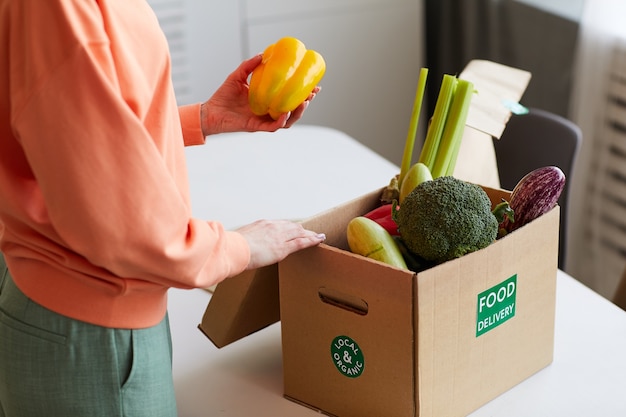 Фото Крупный план молодой женщины, принимающей свежие овощи из коробки на кухне