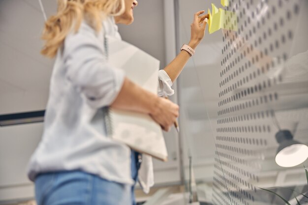 Фото Крупным планом молодой женщины со спиральным альбомом, использующим самоклеящиеся бумажные заметки, работая в современном офисе