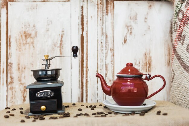 Клоуз-ап старомодной кофейной мельницы и чайника на столе против деревянной стены