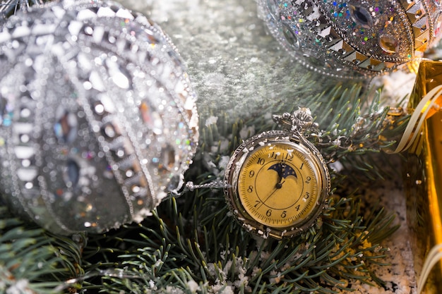 Close up di vecchio orologio da tasca appeso sulla coperta di neve rametti di albero sempreverde decorato con argento scintillante palle di natale