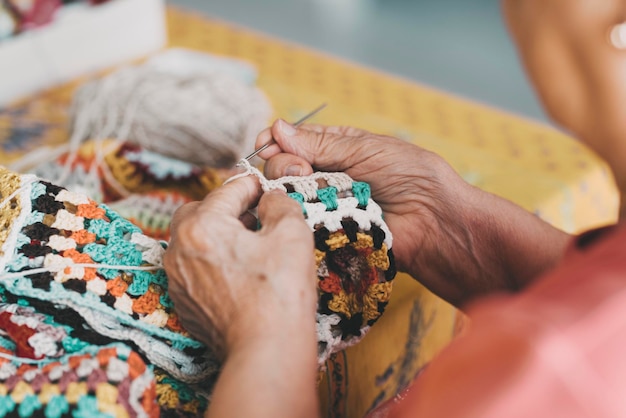Close up of old female hands doing knit work with wool at home for indoor leisure activity Aged retired female people knitting work alone at home Elderly time and fun inside using wool and hobby