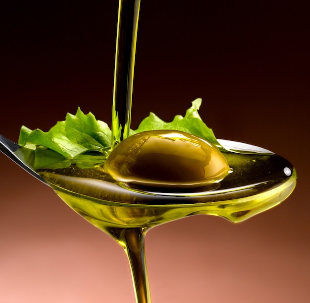 close up of olive oil poured into a spoon over olives and lettuce leaves