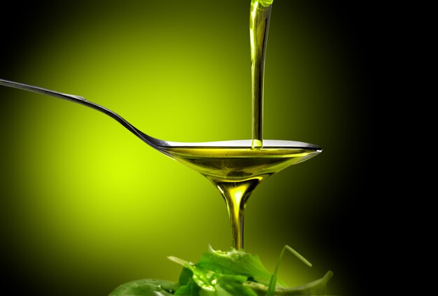 close up of olive oil poured into a spoon over salad