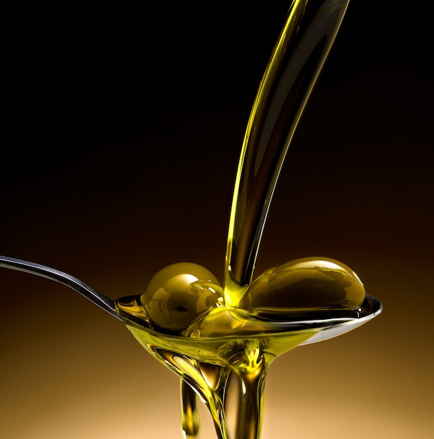 close up of olive oil poured into a spoon with olives