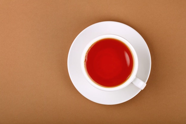 Close up one cup full of red black or fruit tea on white saucer over brown paper, elevated top view, directly above