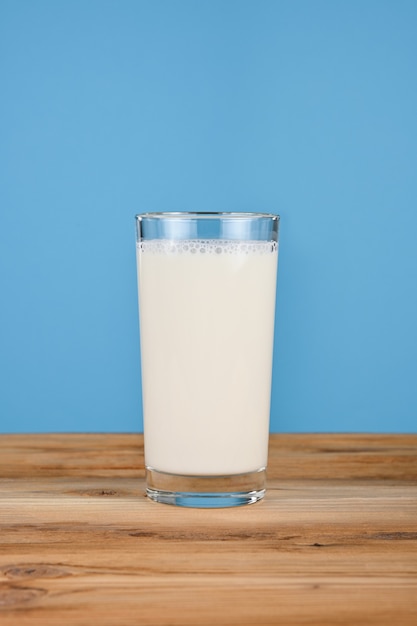 Close up one glass full of fresh milk on wooden table over blue wall, low angle, side view