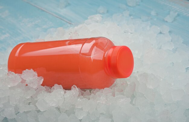 Close up one plastic pet bottle of fresh pink grapefruit juice over background of crushed ice, high angle view