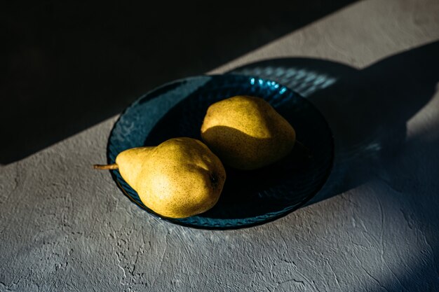 Close up one ripe yellow pear in blue glass plate on grey background modern minimal still life with