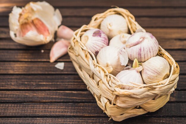 Photo close-up of onions in basket near garlic cloves on wooden plank