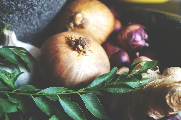 Photo close-up of onions and gingers with leaf vegetables in container