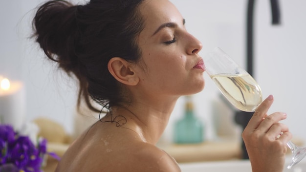 Close-up ontspannen vrouw wijn drinken in bad Sexy meisje ontspannen met een glas witte wijn in badkuip Sensuele vrouw champagne proeven in luxe badkamer