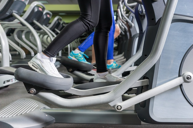 Close-up op benen van mensen die trainen op de crosstrainer-machines in het fitnesscentrum