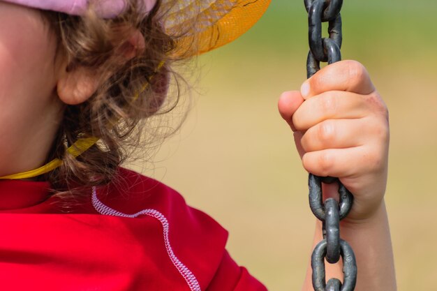 Close-up op de hand van een baby die een kettingkind vasthoudt dat plezier heeft met spelen op een schommel