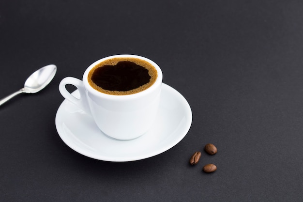 Close-up op de witte kop met zwarte koffie en koffiebonen op de donkere achtergrond