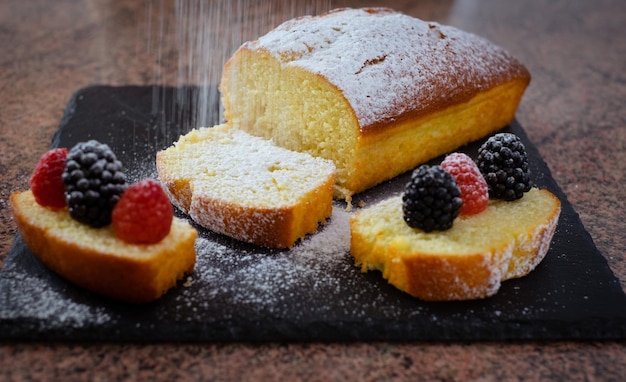 Close-up op de zelfgemaakte pruimentaart rustend op een zwarte stenen snijplank terwijl ze wordt bestrooid met poedersuiker Thuis koken Heerlijk gezond huisgemaakt dessert geserveerd met bessen