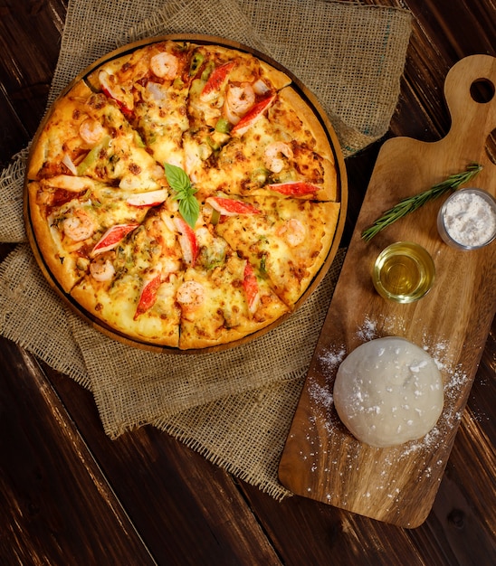 Close-up op deeg, olijfolie, poeder en deegroller voor het maken van zelfgemaakte zeevruchtenpizza met garnalen, krabsticks, paprika's op zak en houten tafel. Voedselconcept.