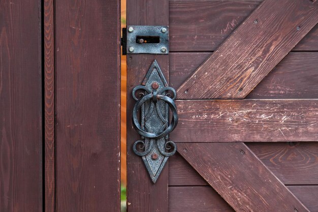 Foto close-up op een decoratief gesmeed handvat en bout in antieke stijl met een gedraaid patroon op een bruine houten deur constructie en decoratie van gebouwen