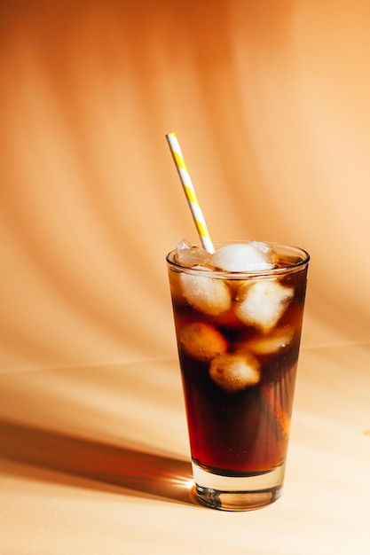 Close-up op een glas met cola en ijs op een beige achtergrond met schaduwen