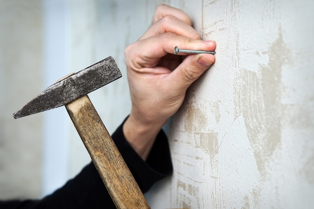 Close-up op een hand die een spijker op een muur hamert met muurschildering Wallpaper. om de foto aan de muur in te lijsten