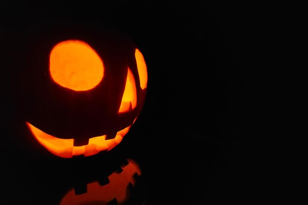 Close-up op een Jack O' Lantern verlicht in het donker en reflecterend op een zwart oppervlak ervoor