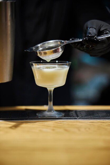 close-up op een metalen zeef waardoor een mannelijke barman een cocktail in een glas giet