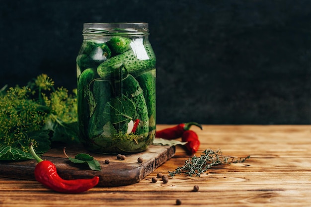 Close-up op een pot gepekelde komkommers met groene kruiden met peper op een houten tafel op een donkere achtergrond