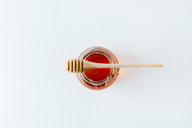 Close-up op een pot honing en een houten spindel voor honing op een witte achtergrond