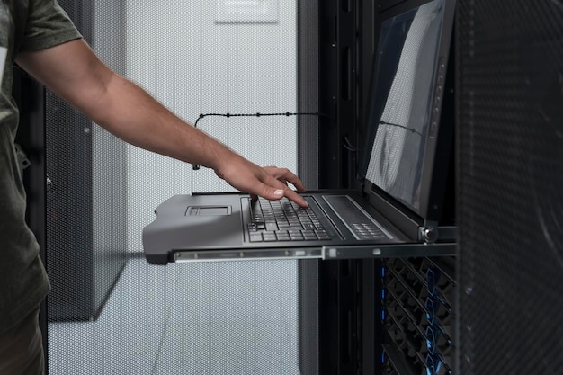 Close-up op handen van Data Center Engineer Toetsenbord gebruiken op een supercomputer. Gespecialiseerde serverruimtefaciliteit met mannelijke systeembeheerder die werkt met een gegevensbeschermingsnetwerk voor cyberbeveiliging.
