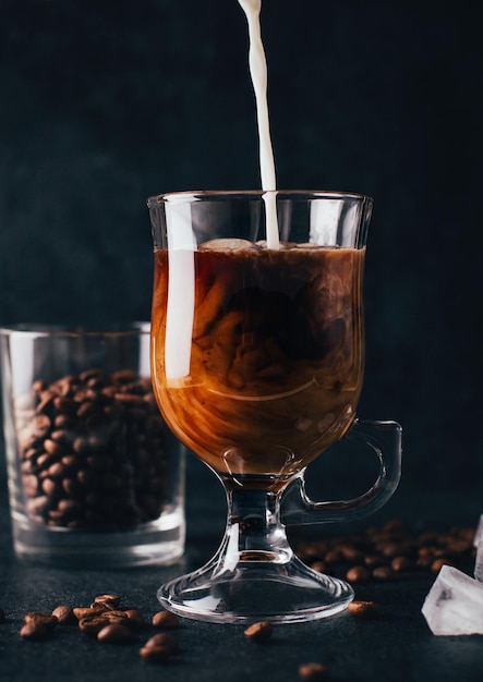 Close-up op koffie met melk in een transparant glas tegen de achtergrond van koffiebonen op een zwarte achtergrond