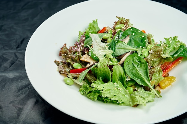 Close-up op salade met spinazie, champignons, paprika, jonge bonen en erwten in een witte kom op een zwarte tafel. Gezond en dieetvoeding. Vegetarisch