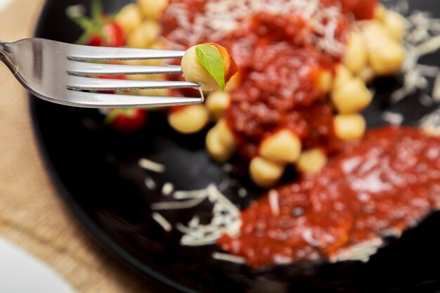 Close-up op vork met gnocchi en bord gnocchi met vage rode saus op de achtergrond