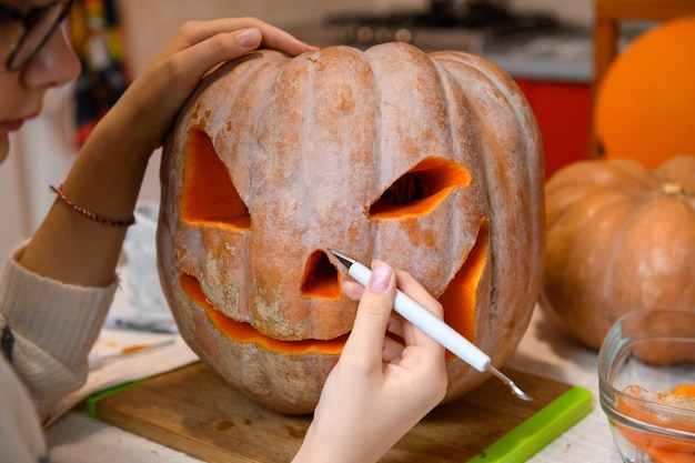 Close-up op vrouwenhanden die mes gebruiken om grote oranje pompoen jackolantern voor halloween-partij te snijden