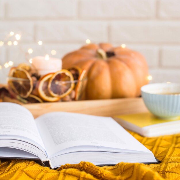 Close-up of open book by pumpkin and coffee cup on tablecloth