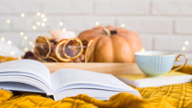 Close-up of open book by pumpkin and coffee cup on tablecloth