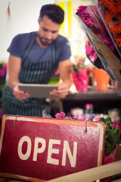 Close-Up of open signboard while of male florist using digital tablet in background