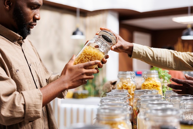 Foto close-up opname van een afro-amerikaanse man die de pasta in de glazen potten bekijkt in een milieubewuste supermarkt een mannelijke klant die naar voedzame bulkproducten kijkt