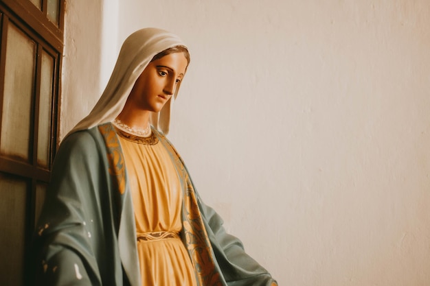Close-up opname van een standbeeld van Maria, de moeder van Jezus, tegen een witte muur