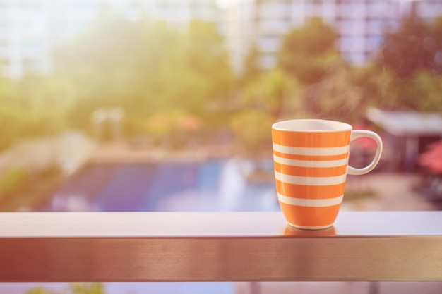 Close up orange coffee cup on balcony of hotel and blurred view of building