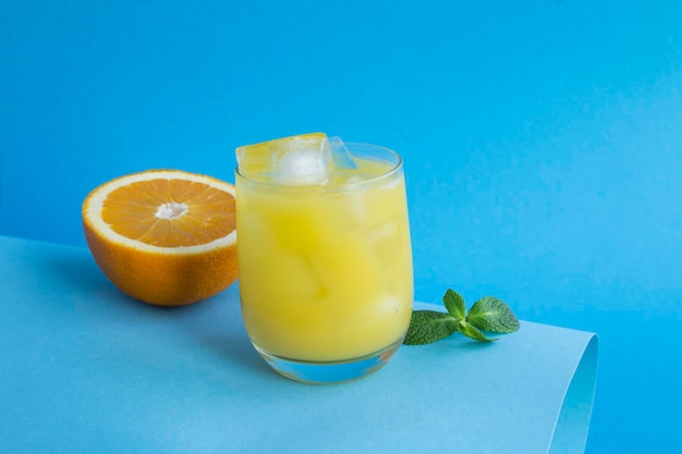 Close-up on orange juice with ice in the drinking glass on the blue background. Copy space.