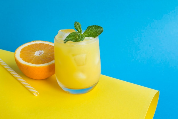 Close-up on orange juice with ice in the drinking glass on the colored background. Copy space.
