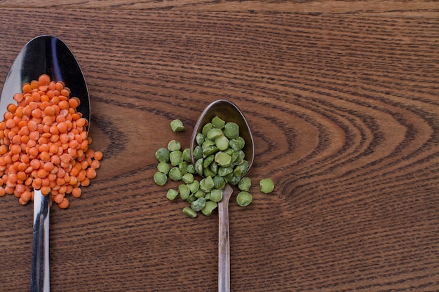 Close up orange lentils and green split peas on metal spoons. Brown wood on background.