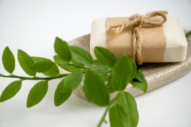 Photo close up of organic natural soap bar wrapped in craft paper lays on tray with aromatic herbs.