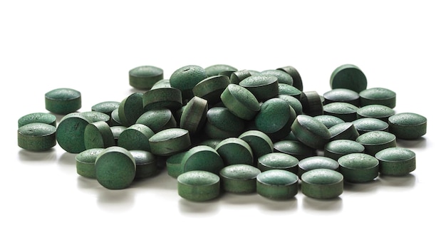 Primo piano di compresse di spirulina organica su sfondo bianco.