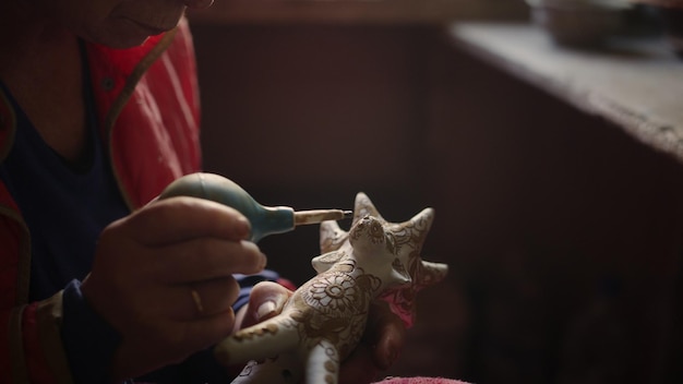Close-up oudere vrouw die puntjes op product in aardewerk zet Senior dame handen versieren speelgoed eland in werkplaats Geconcentreerde keramiek schilderij klei eland in studio