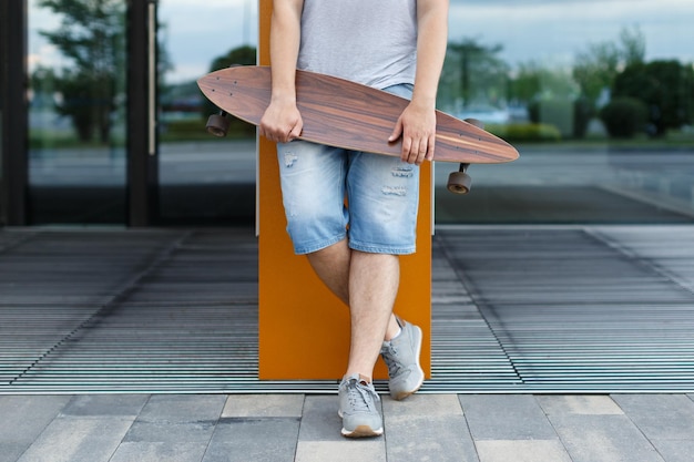 Close-up outdoor portret van jonge man in korte broek en grijze sneakers met longboard in handen