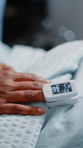 Close up of oximeter on finger of patient with illness in
hospital ward bed. sick woman having tool to measure oxygen
saturation and pulse pressure to cure disease. medical care