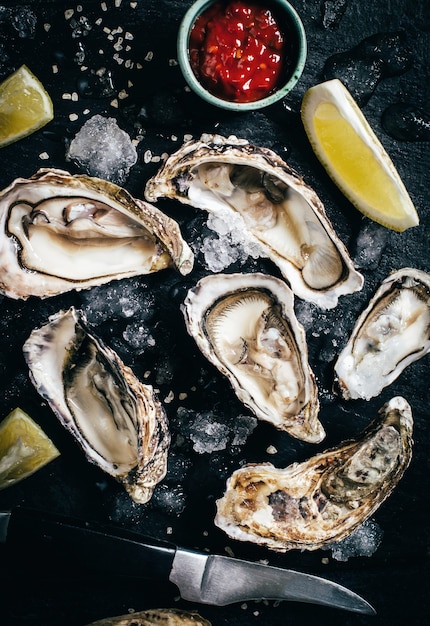 Close-up on oysters with sauce and lemon on a black background top view