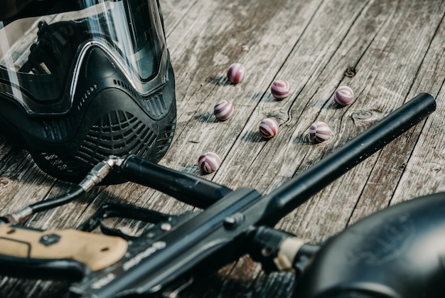 ペイントボール銃、特別なボールと保護マスク、木製のテーブルでペイントボールをするための機器、アクションゲームのコンセプトの接写