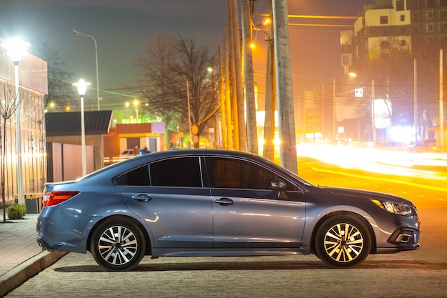 Close up of parked car on roadside at night with blurred view of traffic lights