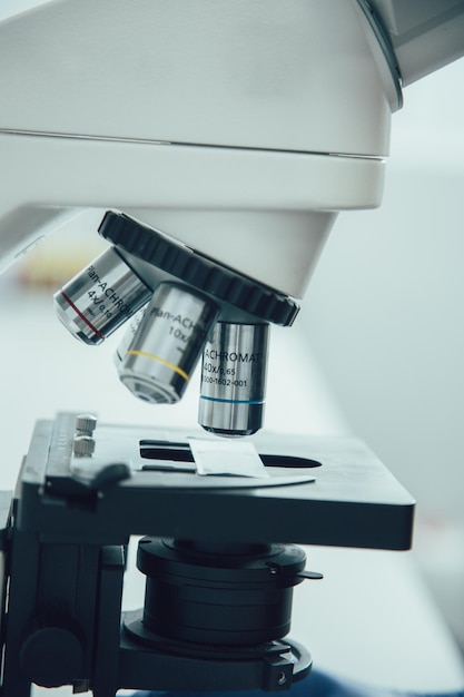 Close up of a part of a microscope in the lab with three\
objective lenses and a glass slide